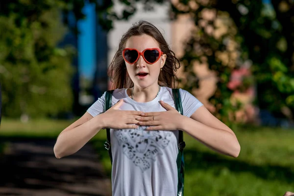 Dziewczyna piękna uczennica. Lato natura po szkole. Okulary, ma kształt serca. Uśmiecha się radośnie. Gesty rąk są w posiadaniu serca. Koncepcja oddech zaskakuje niespodzianka. Emocja korzystających prezent. — Zdjęcie stockowe