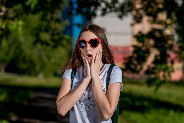 Девочка школьница летом в городе. В очках в форме сердца за рюкзаком. Концепция неожиданного сюрприза. Сюрприз для эмоций . — стоковое фото