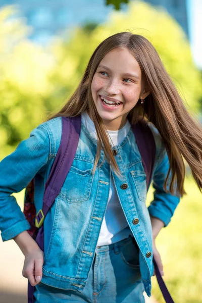 幸せな小さな女の子の子。学校の後の通りの夏。彼女のバックパックの後ろに街の女の子。感情的な喜びのコンセプトです。喜びのジョーク、楽しい感情休日ゲーム. — ストック写真