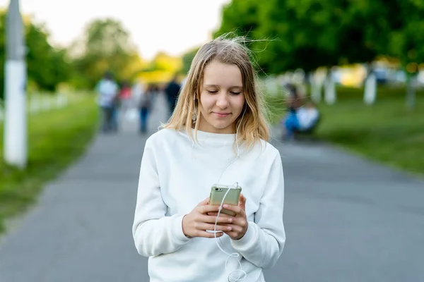 10 代の少女。都市の夏。彼の手でスマート フォンを保持します。インターネット上のビデオを見て音楽を聴きます。ソーシャル ネットワークにメッセージを書き込みます。幸せの笑顔します。. — ストック写真