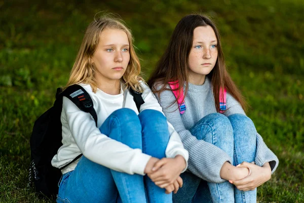 For girl schoolgirl. Summer in nature. They are sitting on grass. Behind backpacks. Rest after school. The concept is best friends. Emotions sadness and frustration, waiting. — Stock Photo, Image