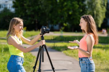 Female student. Summer in nature. The concept of the interview. Emotions of happiness are positive. Record vlog and blog subscribers. Record video lesson for Internet. Use camera with tripod. clipart