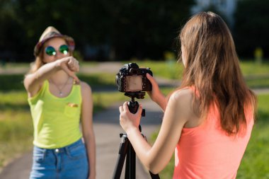 İki kız öğrenciler. Ve yaz doğada. Köle, parmak eller aşağı jest. Kötü bir kavramdır. Kayıt vlog ve blog abone. Internet için kayıt video ders. Kullanma fotoğraf makinesi tripod ile.