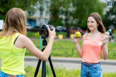 İki kız kız öğrenci kız. Yaz doğa. Kavram sağlıklı beslenme. El şişe su yeşil elma tutar. Kayıt vlog blog abone. Internet için kayıt video ders. Kullanım kamera tripod.