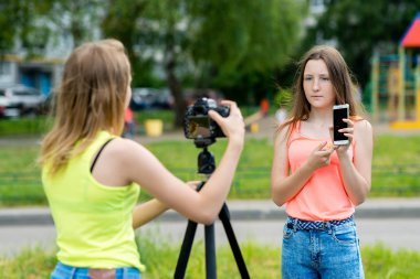 İki kız arkadaş. Yaz doğa. Video kamera için yazar. Elinde smartphone tutar. Genç blogcular kavramı için Internet video kaydediyor. Duygusal mutlulukla gülümsüyor. Gadget'ları hakkında konuşmak.