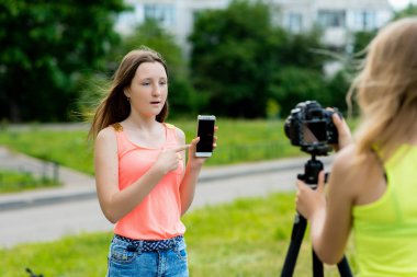 İki kız arkadaş. Yaz doğa. Video kamera yazıyor. Elinde smartphone tutar. Genç blogcular kavramı için Internet video kaydediyor. Duygusal bir konuşma yapar. Gadget'ları hakkında konuşmak.
