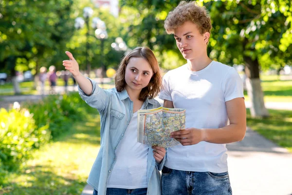 Dziewczyna pokazuje kierunek ruchu człowieka. Lato w przyrodzie. Przechodzień pokazuje gdzie iść do turystów. Młoda para spaceru w parku w mapie drogowej trzymając się za ręce. — Zdjęcie stockowe