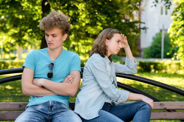 Young couple in summer in park outdoors. Problems in family life. The concept of misunderstanding is a mistrust of insults in a relationship. They sit on a bench in the city. — Stock Photo, Image