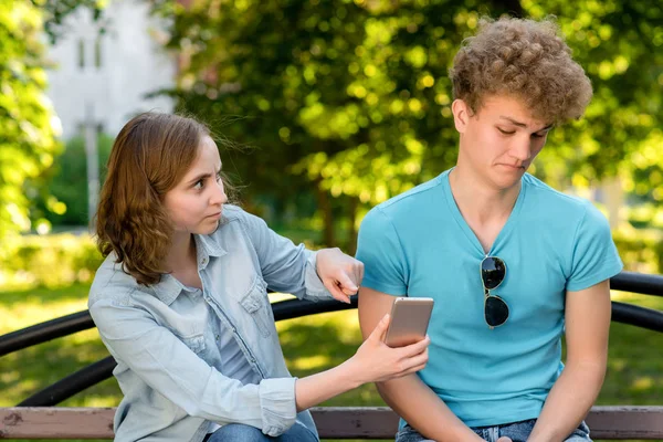 Kluk s holkou na přírodu. Žena ukazuje na smartphone. Chlap se dívá na korespondenci s údivem. Koncepce zrady zrady mladého páru v létě. Problém je ve vztahu. — Stock fotografie