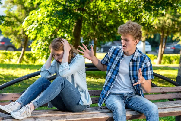 Summer in nature. The guy yells at girl gesturing with his hands. The girl covered her head with hands covering ears. The concept of aggression in a relationship. Scandal in family. — Stock Photo, Image