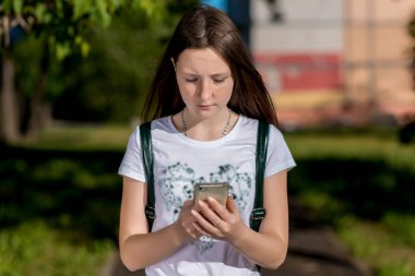 Kız öğrenci. Doğa yazın. Elinde bir akıllı telefon tutar. Bir iletiyi Internet üzerinde yazar. Ebeveynler sosyal ağlar üzerinden iletişim kavramı. Duyguları ile ciddi bir yüz.