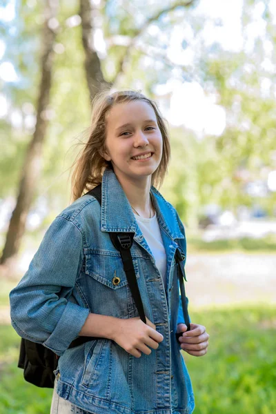 Счастливая девочка-подросток улыбается. Лето на природе. Школьница в отпуске. В джинсовой куртке за рюкзаком. Эмоции любви и счастья . — стоковое фото