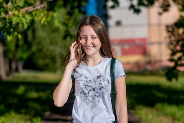 Una colegiala. Verano en la naturaleza después de clases escolares. En sus manos tiene un smartphone. Habla por teléfono. Feliz sonrisa. Disfruta de relajarse en la naturaleza . —  Fotos de Stock