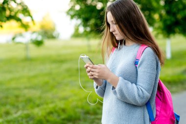 Kız kız öğrenci genç. Yaz doğa. Smartphone sırt çantası arkasında tutarak ellerinde. İletileri sosyal ağlar yazar. Internet üzerinde iletişim kavramı. Duygu ciddi bir yüz. Metin için boş alan.