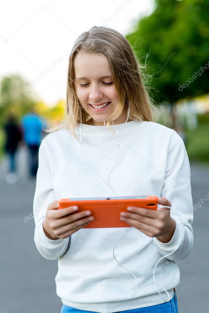 Girl schoolgirl teenager. Summer in nature. Hands holding a tablet. The concept of watching videos from social networks. Emotion happy enjoys listening to music on Internet.