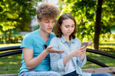 Genç çift öğrenci. Bir adamla bir kız yaz park doğa. Şehirde bir bankta oturuyorlar. Elinde bir akıllı telefon tutar. Sürpriz duyguların. Kavram hayal kırıklığı sonuç hayal kırıklığı olduğunu.