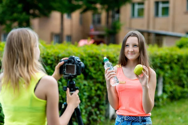 Dos adolescentes. Verano en la naturaleza. En sus manos tiene una botella de agua y una manzana. El concepto de alimentación saludable. Jóvenes bloggers graban video para sus suscriptores . — Foto de Stock