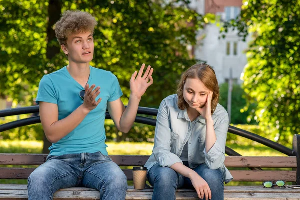 La chica estaba cansada de hablar. El tipo está hablando con la chica. Reticencia a escuchar al interlocutor. Un tipo con una chica en verano en un parque en la naturaleza. Problemas en la relación. Adolescentes difíciles . —  Fotos de Stock