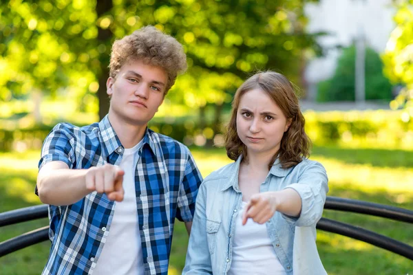 Joven pareja chica y novio. En el verano en el parque en la naturaleza. Se sientan en un banco en la ciudad. Hace gestos con los dedos hacia el marco. El concepto que va a hacer frente. Emociones de confianza en sí mismo . —  Fotos de Stock