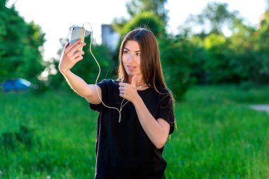Sosyal ağlarda iletişim kurar. El hareketi gibi onay gösterir. Mutlu yaz aylarında parkta gülümseyen genç esmer kadın. Görüntülü arama duygusal iletişim.
