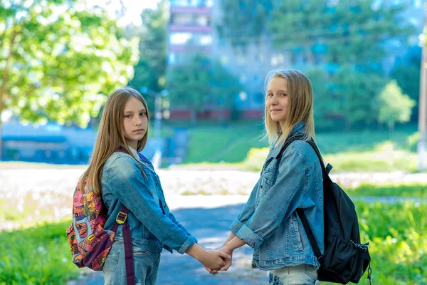 Två flickor Skolflicka. Han håller varandras händer. Bakom ryggsäck. Kläder jeans. Konceptet är bättre än skolan vänskap. Ler lyckligt. — Stockfoto