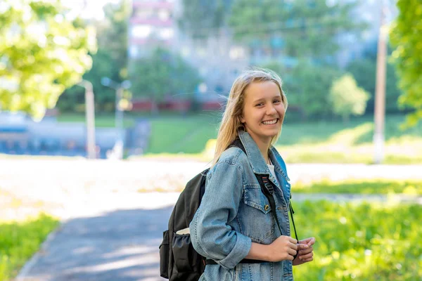 Nastolatkę. Latem w parku. Za plecak. Koncepcja wkrótce do szkoły. Ilość wolnego miejsca dla tekstu. Emocja usmiecha. — Zdjęcie stockowe