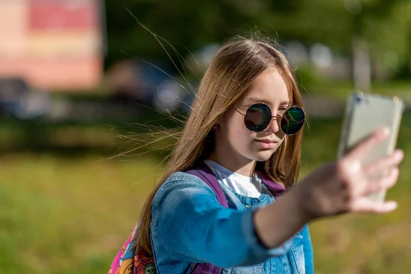 Une adolescente. L'été dans la nature. Dans ses mains tient un smartphone dans des lunettes de soleil. Faire une photo du réseau social. Espace libre pour le texte . — Photo