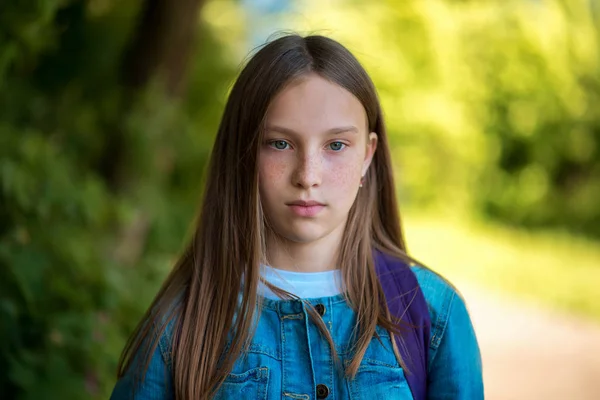 Detail dívky, školačka. Léto v přírodě. Na sobě džíny v oblečení. Dlouhé vlasy pihy na obličeji. Emoce, koncentrace pozornosti. — Stock fotografie