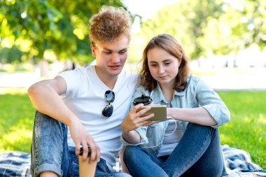 Kız adamla bir battaniye üzerinde oturuyor. Doğa yazın. Bir bardak kahve ve çay holding eller. Smartphone vasıl görünüyorlar. Tarassut video kırpmak müzik dinliyor. Şehir dışında dinlenme.