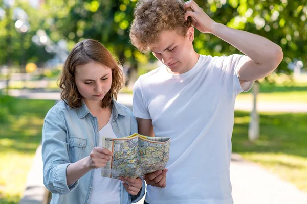 Un tipo con una chica en verano en la ciudad en la naturaleza. En sus manos tiene una hoja de ruta. Perdí la dirección. Él no sabe a dónde ir. El concepto de malentendido. Él no sabe a dónde ir. . —  Fotos de Stock