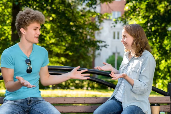 Ein Kerl mit einem Mädchen im Sommer in einem Park in der Natur. kommuniziert emotional mit Gesten. lächelt glücklich. Zelten. gekleidet in lässiger Kleidung. — Stockfoto