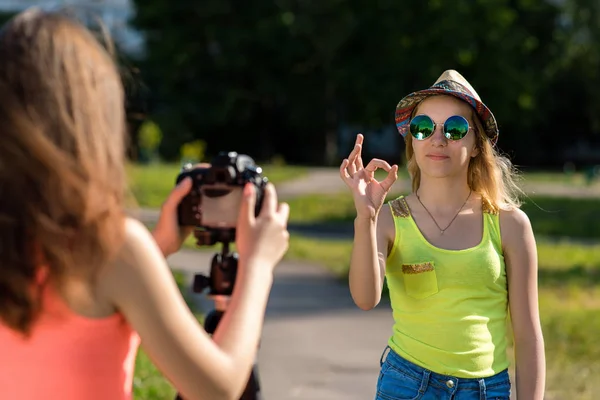 Dvě holky jsou kamarádky. V létě v městě. Nahrávat video na kameru. S gestem rukou ukazuje cca Sluneční brýle a klobouk. — Stock fotografie