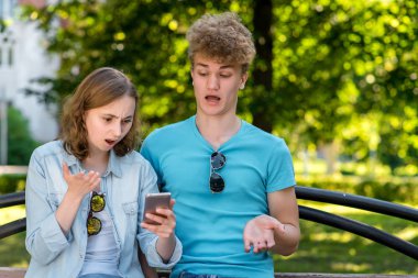 Adam bankta kızla. Doğa yazın. Elinde bir akıllı telefon tutar. Sürpriz duyguların. Ne oluyor bir yanlış anlaşılma. Hayal kırıklığı kavramı.