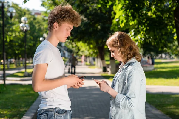 Chlapec a dívka se čelem k sobě. Léto v přírodě. Ve svých rukou drží smartphone. Emoce, Seznamka v parku. Pojem datování v přírodě. Ten se seznámí s dívkou. — Stock fotografie