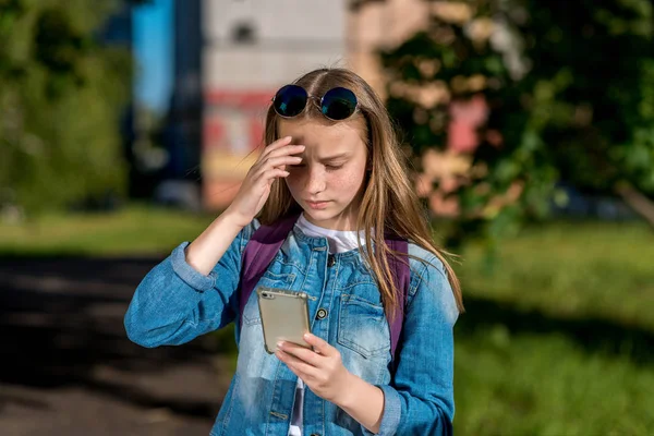 Девочка-подросток. В летнем городе. В его руках смартфон. В джинсовой одежде, солнечных очках. Понятие неожиданности, разочарования, а не желания. Эмоции недопонимания, вдумчивый . — стоковое фото