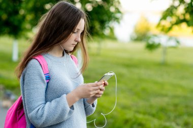 Kız kız öğrenci öğrenci. Sokakta yazın. Elinde bir akıllı telefon tutar. Müzik çalma okur ve sosyal ağlar üzerinde iletileri yazar. Metin için boş alan.
