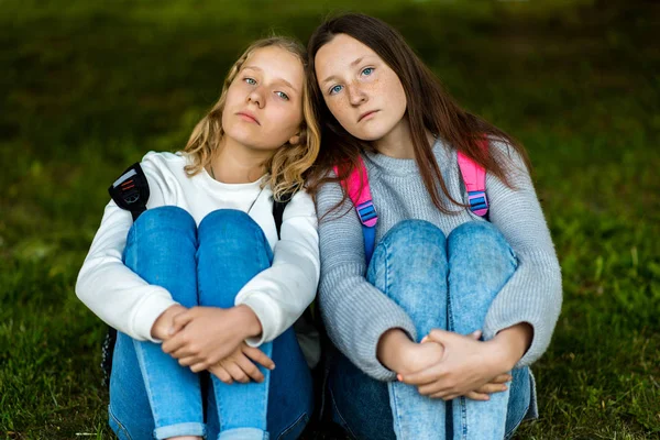 Deux écolières. L'été dans la nature. Ils sont assis sur l'herbe. Il se repose après l'école. Le concept est meilleur ami. Les émotions se reposent après une dure journée . — Photo