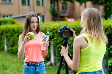 Kız kız öğrenciler için doğada yaz. Sağlıklı beslenme hakkında bir video kayıtları. Elinde bir yeşil elma ve bir şişe su tutar. Internet için kayıt video ders. Kullanma fotoğraf makinesi tripod ile.