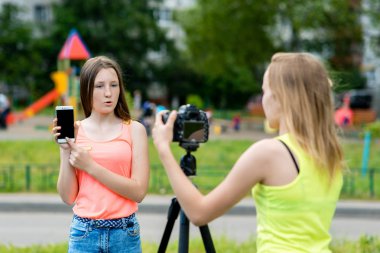 İki kız arkadaş, doğada yaz. Belgili tanımlık smartphone ile ilgili bir video kaydeder. Elinde telefon tutar. Kayıt vlog ve blog. Internet için kayıt video ders. Kullanma fotoğraf makinesi tripod ile.