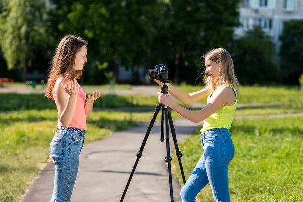 Όπου λίγο έφηβων κοριτσιών το καλοκαίρι στο πάρκο εγγραφής βίντεο στη φωτογραφική μηχανή. Συναισθηματικά gesticulates με το χέρι χρησιμοποιώντας μια φωτογραφική μηχανή με τρίποδα. — Φωτογραφία Αρχείου