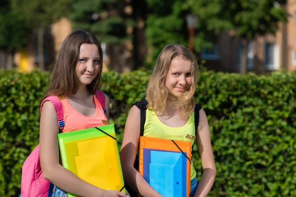 放課後公園で夏に 2 人の女の子女子高生の代。両手のバックパックの後ろにノートブックのフォルダー。学校に戻ってのコンセプトです。幸せと顔に笑顔の感情. — ストック写真