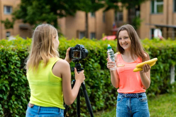 Holky kamarádky v létě v parku zaznamenává video na kameru ve zdravé stravě. Ruce drží banán láhev vody šťastně a spokojeně usmívá. — Stock fotografie