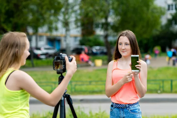 Dvě holky kamarádky, v létě v parku v přírodě. V rukou drží smartphone vypráví o nových funkcích. Píše video na kameru. — Stock fotografie