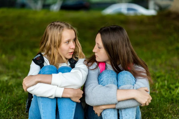 Two schoolgirls teenage girl sitting on grass in summer in the park. The concept is best friends, resting in the city after the lessons. — Stock Photo, Image