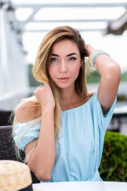 Mavi elbiseli, bir kafede yaz aylarında güzel kız poz. Güzel tabaklanmış deri ve uzun saç. Duygusal olarak saç, bakışları düzeltiyor. İş kadını tatil.