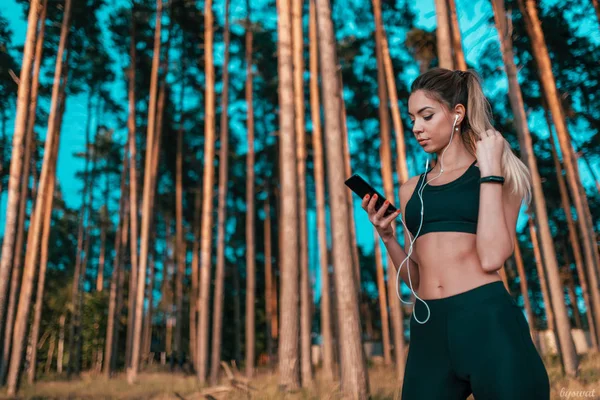 Gadis di hutan itu melihat teleponnya. Olahraga luar ruangan . — Stok Foto