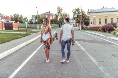 Genç çift görünüme geri, yaz aylarında şehrin içinden git. Kaykaylar, longboards, temiz havada yürüyüş ruqas içinde tutulur. Beyaz vücut mayo, bir t-shirt ve kot giyen bir kız.