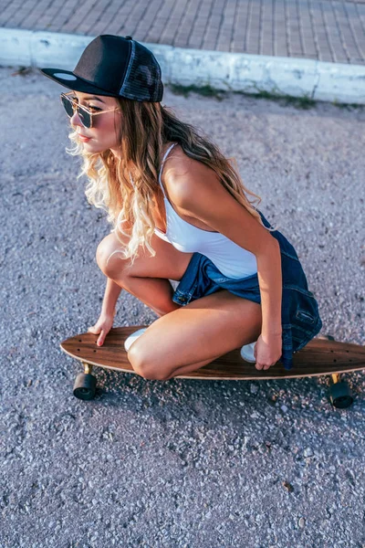 Seorang gadis dalam pakaian renang, naik skateboard di longboard, rambut panjang, kulit kecokelatan, kacamata hitam. Terhadap jalan aspal. Konsep rekreasi pemuda di kota. Wanita Kaukasia Eropa yang cantik. . — Stok Foto
