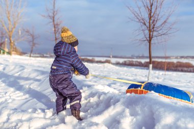 Küçük bir çocuk 3 yıllık eski mavi tulum, boru bir slayttan sürükledi. Kış mevsiminde, açık havada, doğada dinlenme.