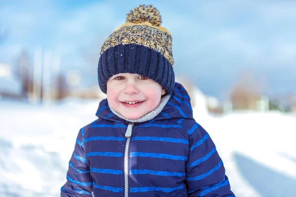 3 yaşında küçük bir çocuk portresi. Temiz havada kışın yakın çekim. Açık rekreasyon gülümseyen mutlu. Mavi bir ceket ve sarı bir şapka.